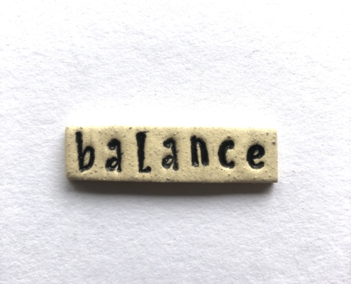 A small ceramic tile with the word balance written in it.