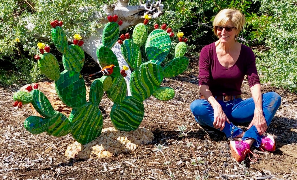A woman kneeling down next to a cactus.